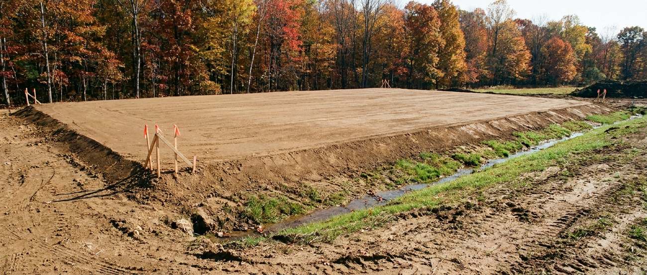 Freshly graded residential lot with smooth bare earth sloping away from a foundation line
